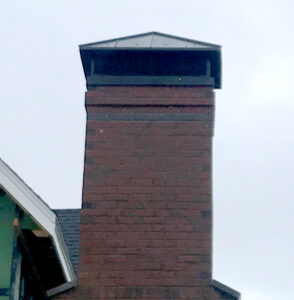 Top of a red brick chimney showcasing a newly installed dark metal chimney cap, representing a completed chimney repair project.