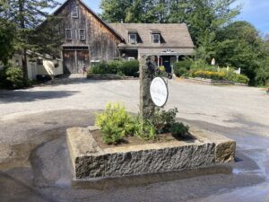 Summer view of a historic inn with a large barn, and a newly installed central granite planter in the paved driveway area.