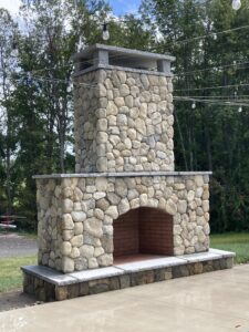 Large outdoor stone fireplace with red brick firebox and string lights overhead.